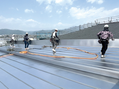 揚重した長さ15mの屋根材を数名で運ぶ。多い時は1日25名くらいが作業に当たる